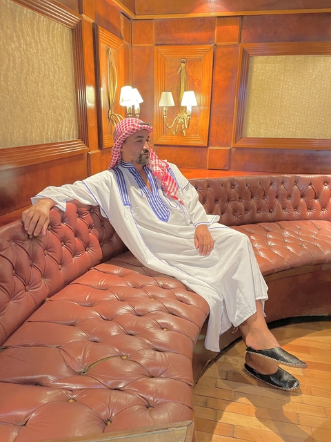 Person seated indoors on a tufted couch in traditional attire.