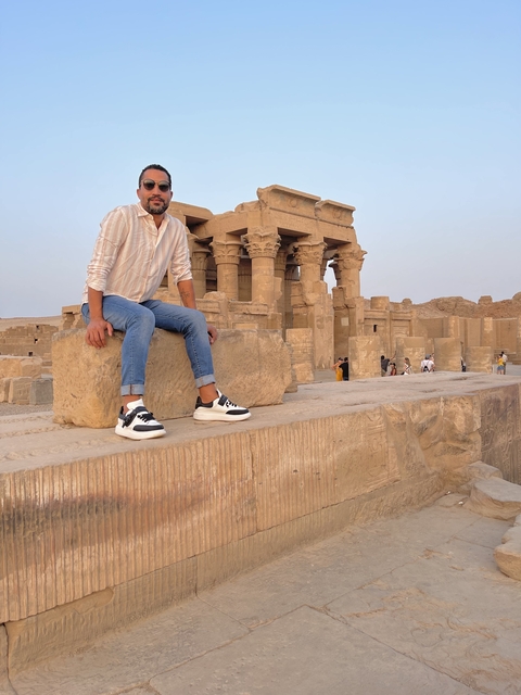 Person sitting on ancient ruins with others in the background.