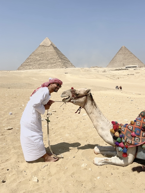 Person smiling with a camel by the pyramids.