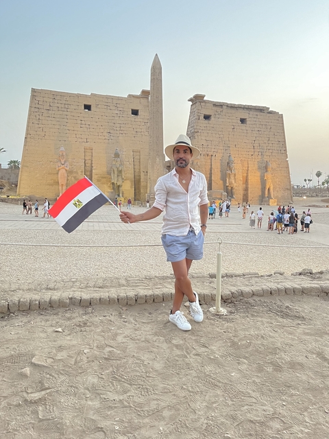 Person holding Egyptian flag with temple ruins in the background.