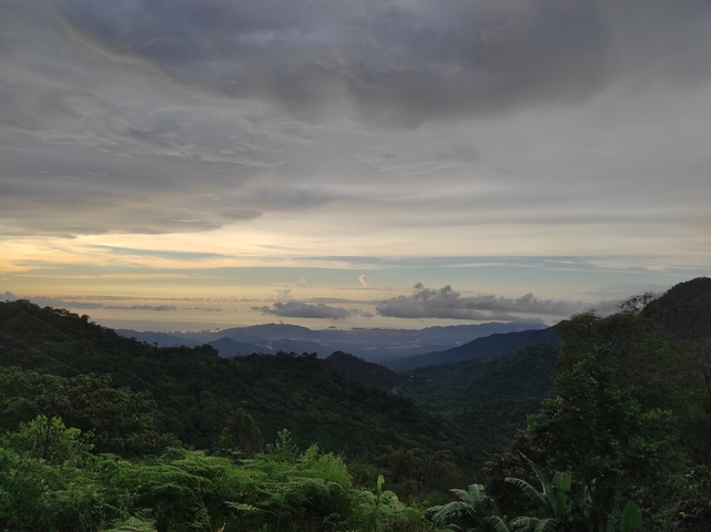 Wide view of a valley with clouds over the sea.