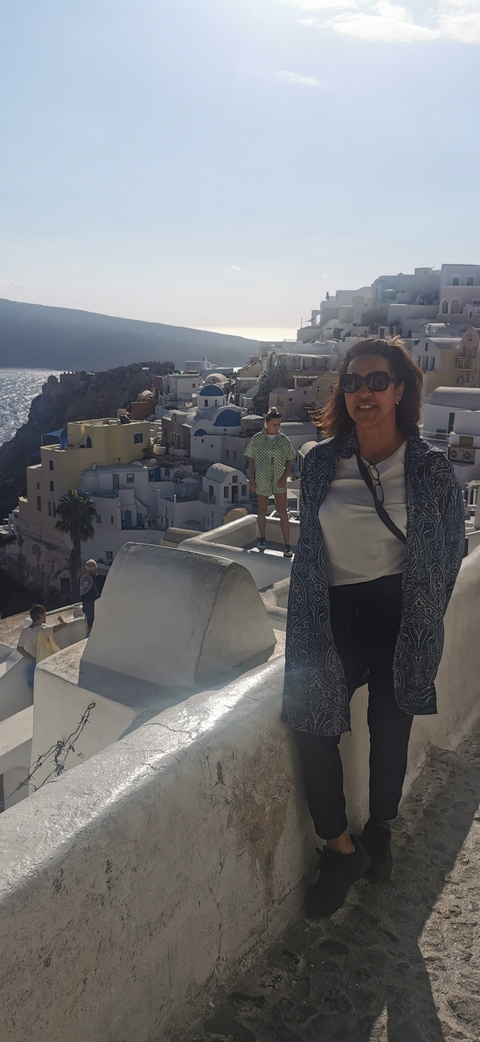 Tourist smiles with the iconic white houses of Santorini cascading down the cliff behind her.