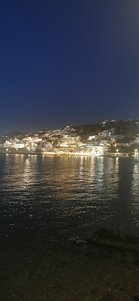 Night view of Mykonos town lights reflecting across the harbor’s dark water.