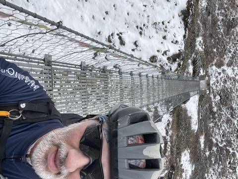 Person in helmet on suspension bridge in snowy area.