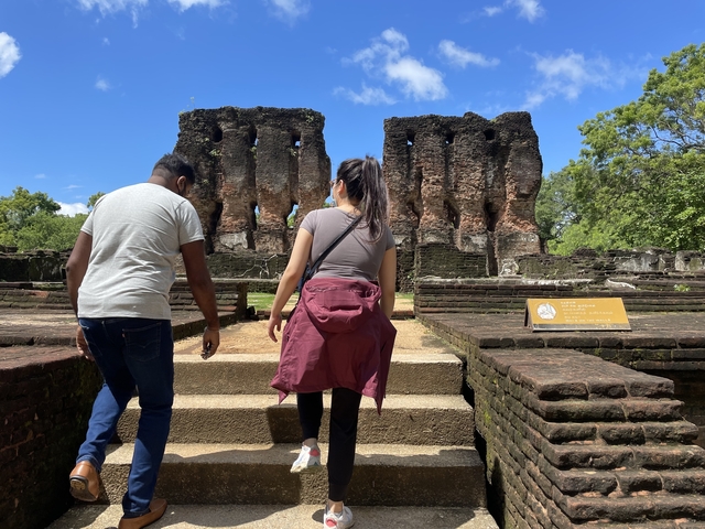 Two visitors walk toward ancient brick ruins at Polonnaruwa on a sunny day