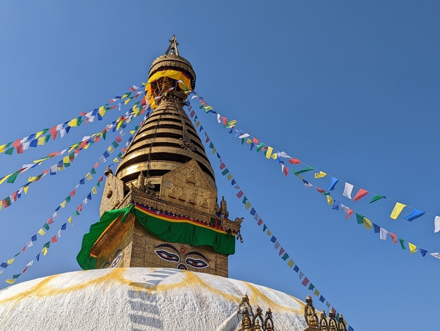 A stupa with prayer flags against a blue sky.