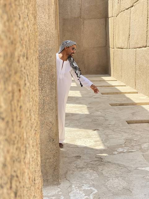 Person in traditional attire posing beside stone walls.