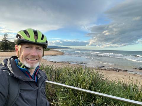 Sideways photo of a beach with a person and greenery.