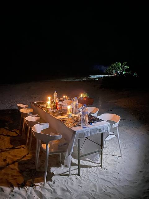 Table with candles and dining setup on the beach at night.