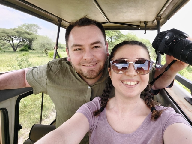 Couple smiling inside a safari vehicle with greenery outside.