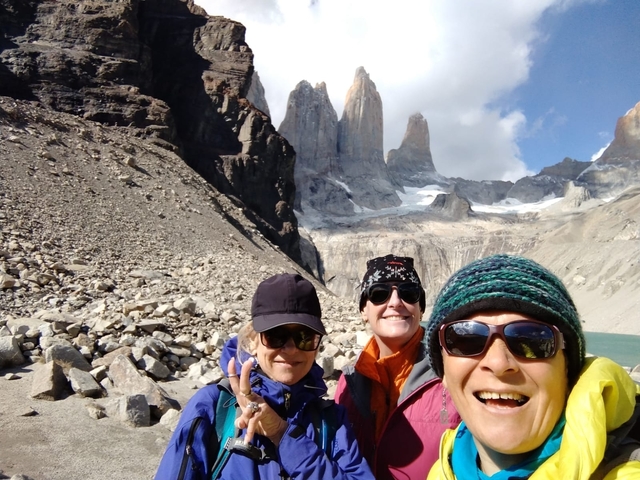 Three hikers pose with smiles in front of the dramatic granite spires and glacial lake of Torres del Paine