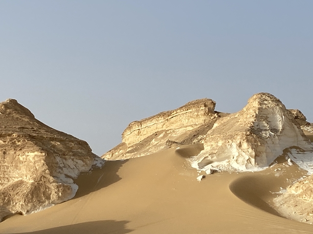 Rocky desert landscape with sandy dunes and clear sky.