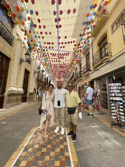Two people posing under hanging decorations in a street.