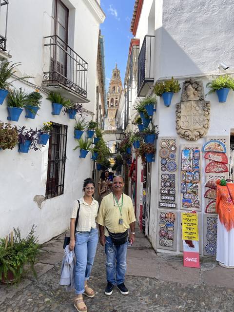 Two people posing in a colorful street lined with pots and souvenirs.