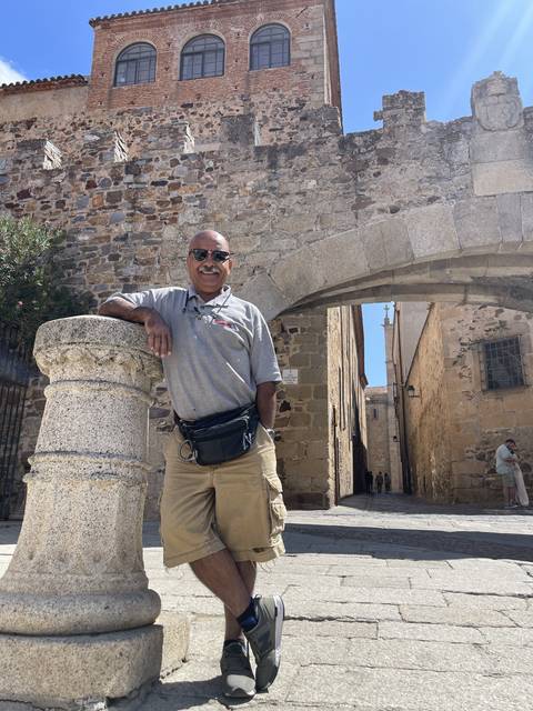 Person leaning on a stone structure with historic buildings.