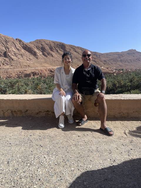 Two people sitting on a stone ledge with mountainous landscape.