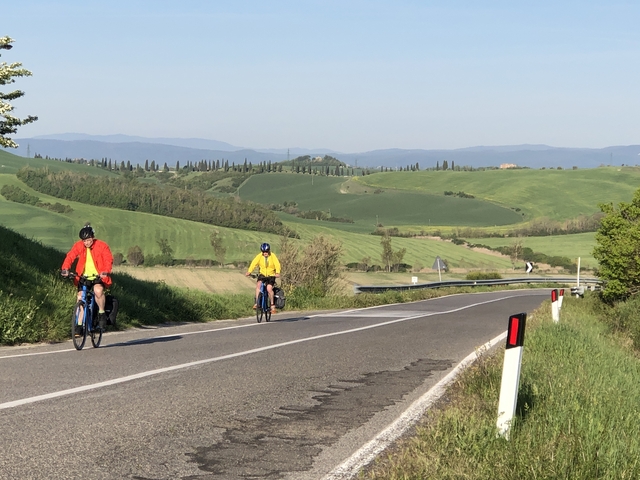 Two cyclists riding on a rural road with scenic green hills.