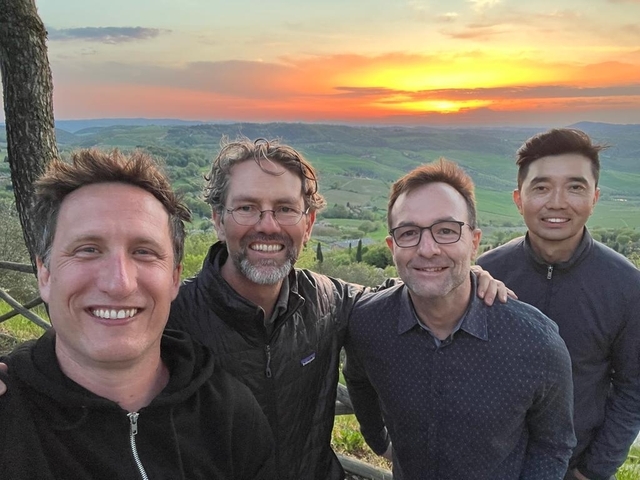 Four men posing during sunset with a scenic landscape backdrop.