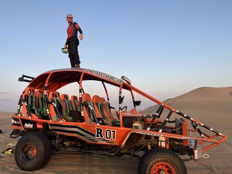Person standing on a dune buggy in a desert landscape.