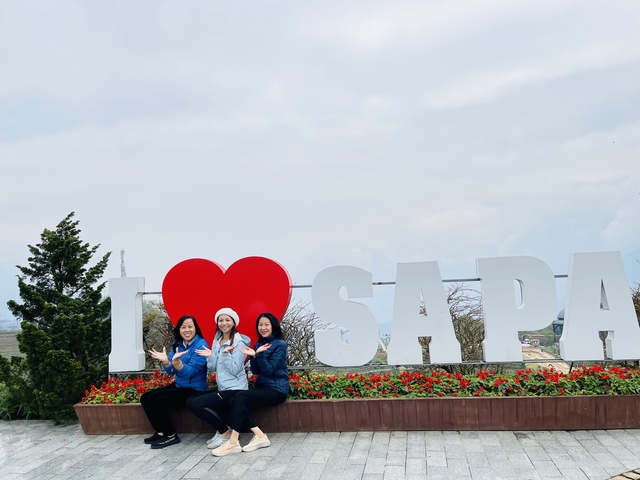 Three women posing with an 'I Love Sapa' sign in a scenic setting.