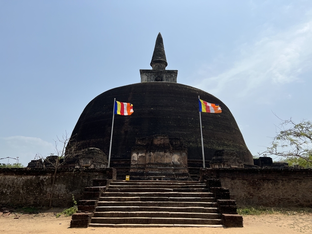 A large stupa with two flags in front under a blue sky.
