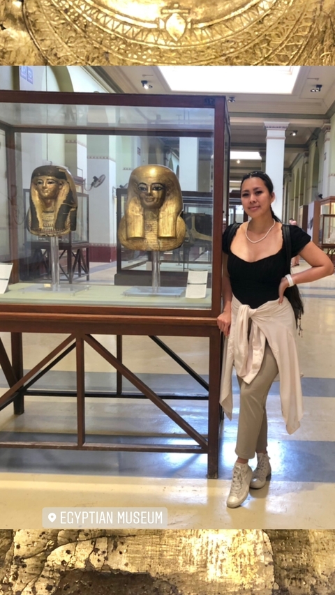 Woman posing in front of an Egyptian sarcophagus in a museum.