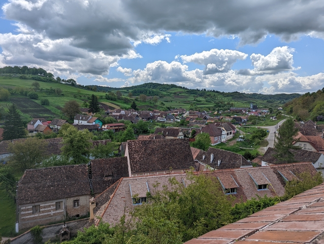 Panoramic view of a village with red-tiled roofs and green hills.