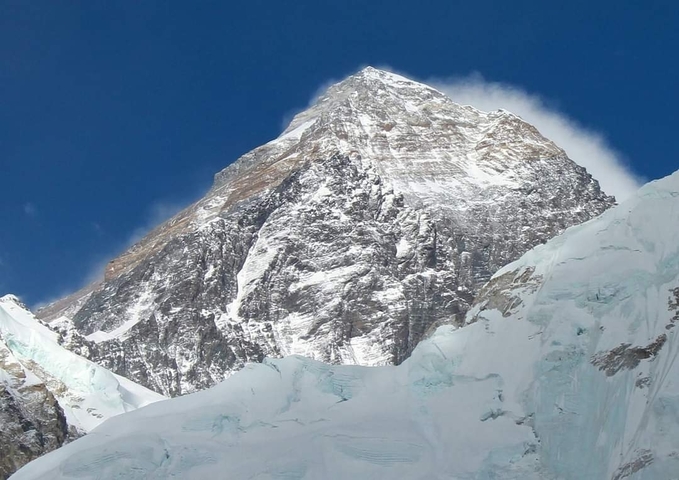 Snow-covered pyramid face of Mount Everest sharply rising against a deep blue sky