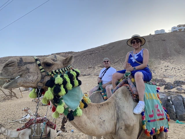 Two people riding camels in a desert landscape.