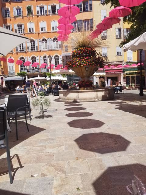 Outdoor plaza with vibrant pink umbrellas, buildings and people seated at tables.