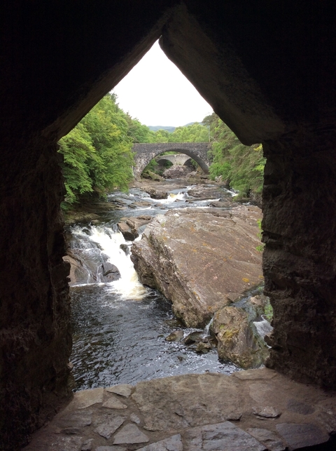 Ancient stone bridge over a river flowing through a forest.
