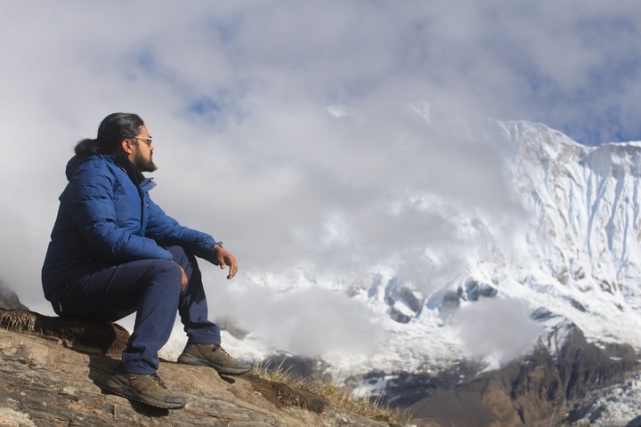 Hiker sitting on a rock looking at snowy Himalayas.