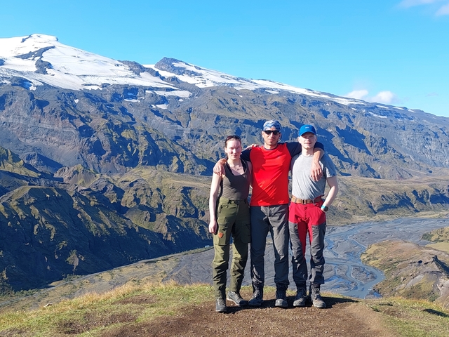 Three hikers standing together in front of a mountainous backdrop.