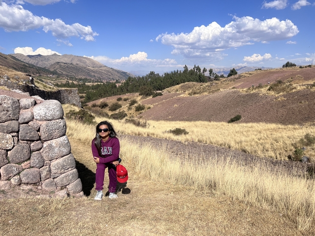 Person sitting next to a stone wall with open landscape.