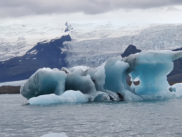 Iceberg floating in a lagoon with a glacier in the background.