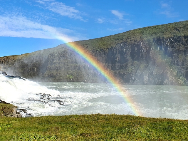 Rainbow over a waterfall with rugged cliffs.
