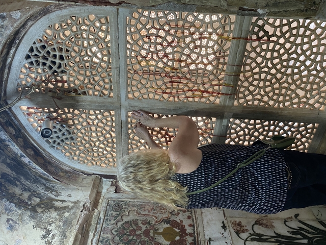 Woman tying threads on a lattice screen.