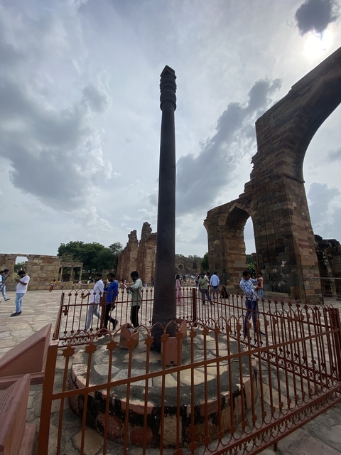 People walking around ancient ruins with a tall iron pillar.
