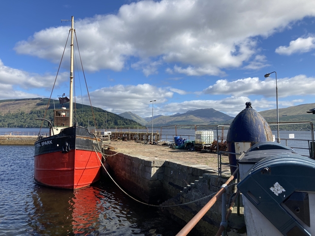 Red boat moored to pier with hills in the background.