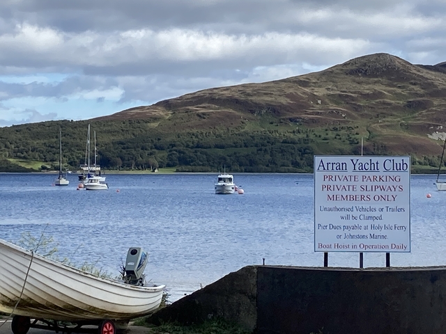 Sign for a yacht club with boats and hills in the background.