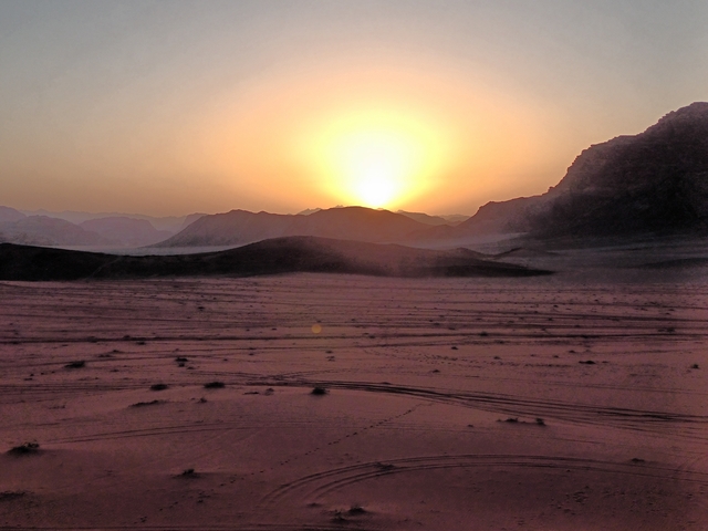 Sunset over a desert landscape with silhouetted mountains.