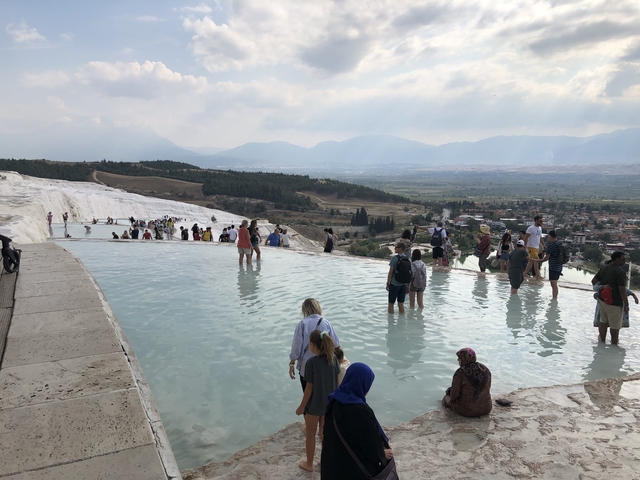 Tourists enjoying thermal pools with mountains in the background.