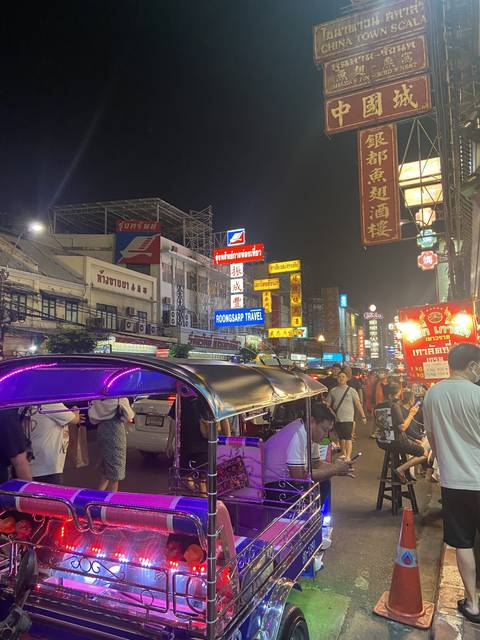 Busy night street with neon lights and tuk-tuks.