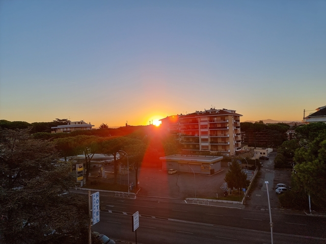 Sunset over buildings and trees in an urban area.
