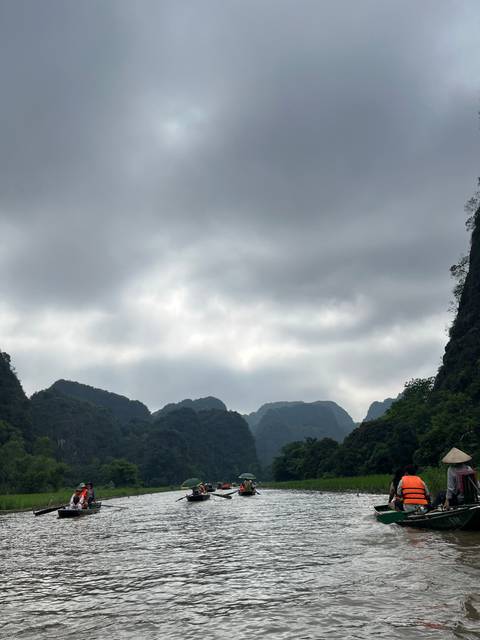 Rowboats on a river with mountains under a cloudy sky.