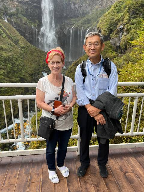 Two people posing on a bridge with a waterfall in the background.