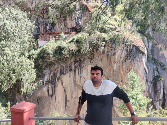 Person posing near a cliff with a temple in the background.