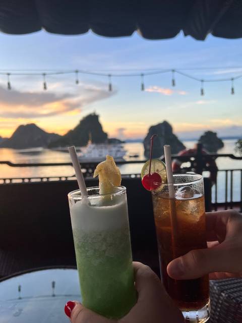 People holding cocktails on a boat during sunset.