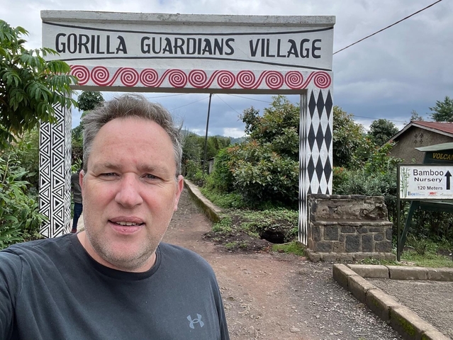 A man taking a selfie in front of a sign saying 'Gorilla Guardians Village'.