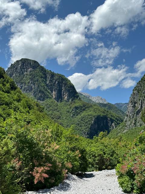 A lush green mountain landscape with blue sky and white clouds.